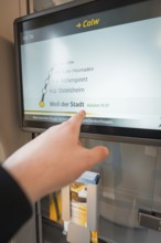 Hand points at a display with timetable and departure times on the train, battery electric train