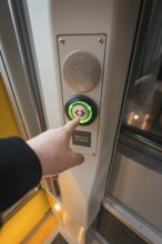 Person presses on the green door button of a modern train, Siemens Micro Plus B battery electric
