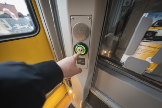 Hand presses the illuminated door button on the yellow train door, battery electric train Siemens