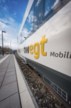 View along the rail of a white-blue train with MOVING branding under a blue sky, Siemens Micro Plus