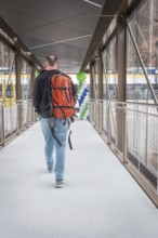 Man with orange backpack walks across a glazed transition with balloons, battery electric train