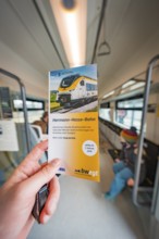 Hand holding brochure about the Hermann-Hesse railway inside the train, battery electric train