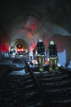 Firefighters walk on tracks through a dark tunnel with red light effects, fire drill on the Hermann