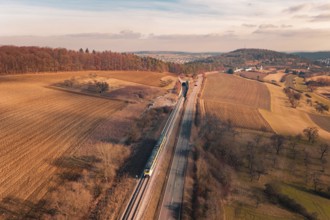 Wide landscape with railroad tracks and a distant train, surrounded by fields and forests, fire