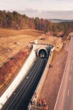 Train is just entering a railway tunnel surrounded by landscape and trees in aerial view, fire