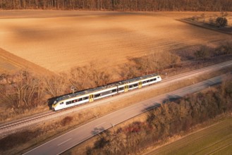 Train travels along railroad tracks between fields and forest at sunset, fire drill on the