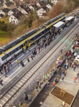 People stand close to the platform while a train stops in a village, opening of the Hermann Hesse