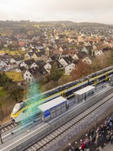 Train stops at a train station in a small town with many spectators and houses in the background,