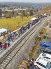 People stand next to parked cars at a railway station in rural surroundings, opening of the Hermann