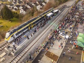 Large groups of people receive a train on the platform, surrounded by city and nature, opening of