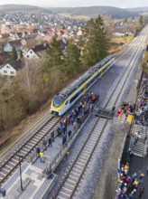 A train stops at a platform surrounded by a crowd of people. In the background you can see a