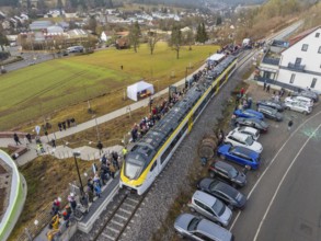 Train at a train station with people waiting and parked cars in a rural urban landscape, opening of