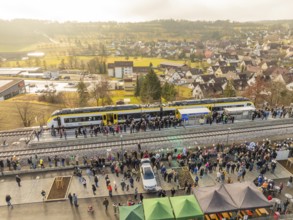 Numerous people at a village train station, festive atmosphere upon arrival by train, opening of