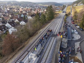 View of railway line with people next to an urban housing estate in a hilly landscape, opening of
