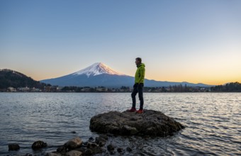 Young man standing on rocks in Lake Kawaguchi, view of Mount Fuji volcano at sunset, Yamanashi