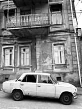 Monochrome, vintage car standing in front of a Nostaligian building with a distinctive balcony,