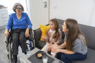 Granddaughter and mother enjoying a family visit with elderly grandmother sitting in a wheelchair,