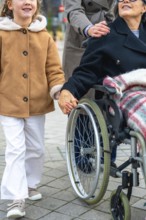 Granddaughter walking alongside her grandmother in a wheelchair, holding hands, with a woman