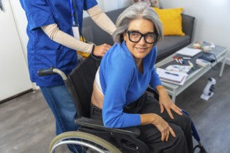 Senior woman in a wheelchair smiling and looking at camera while a professional nurse or caregiver