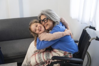 Granddaughter embracing elderly grandmother with gray hair and glasses. Sitting in a wheelchair.