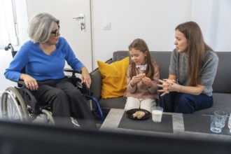 Grandmother in a wheelchair interacting with her family, including a young girl eating a snack and