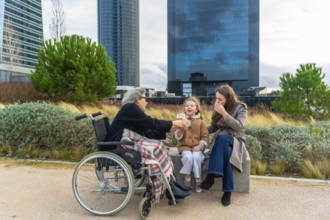 Grandmother in wheelchair enjoys a snack from her smiling granddaughter while family relaxes