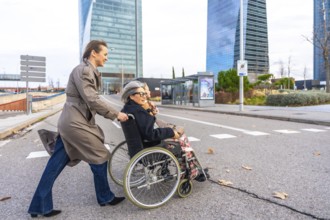 Daughter pushing a happy elderly woman in a wheelchair, moving along a modern city street with