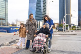 Family members and a professional caregiver are walking outdoors with a smiling senior woman in a