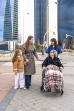 Family members and a caregiver are walking with an elderly woman in a wheelchair, providing care