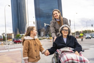 Three generations walking in the city, grandmother in a wheelchair, daughter pushing and