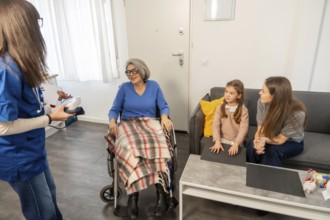 Nurse communicating with an elderly woman in a wheelchair, while her daughter and granddaughter are
