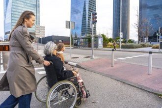 Young woman pushing elderly grandmother in a wheelchair while a child walks beside them across a
