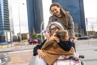 Multi generational family group spending time together outdoors, with a daughter pushing her mother