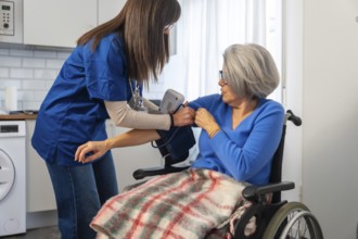 Healthcare professional in blue scrubs measuring an elderly woman's blood pressure in a wheelchair