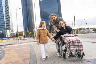 Multi generational women sharing a city walk, grandmother in wheelchair holding granddaughter's