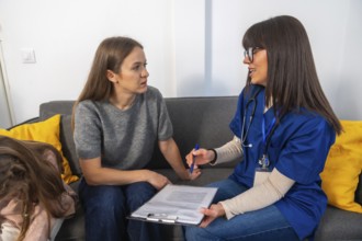Nurse in scrubs with stethoscope consults a woman at home, explaining medical options and paperwork
