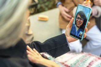 Senior woman in a wheelchair having a video call with a younger family member on a smartphone while
