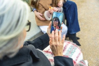 Elderly woman in a wheelchair using a smartphone for a video call with a smiling relative, staying