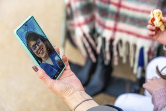 Hand holding a smartphone displaying an elderly woman on a video call, staying connected with a