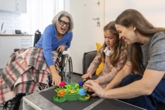 Senior woman in a wheelchair. Her daughter. And granddaughter happily playing a hungry hungry
