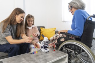 Granddaughter and mother playing with a microscope and colorful hourglasses at home while a senior