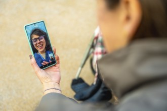 Person holding smartphone showing video call with smiling woman while pushing a wheelchair