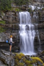 Young pretty hiker standing on rocks in front of Cascata di Mezzo waterfall, long exposure,