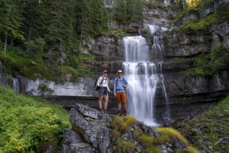 Two hikers standing on rocks in front of Cascata di Mezzo waterfall, long exposure, Vallesinella,