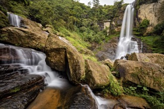 Two waterfalls flow between large rocks in a lush, green jungle, waterfall in the mountains of