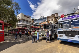 People gather under clear skies at a bus stop surrounded by buses, Kandy bus station in Sri Lanka