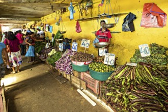 A market area with various types of vegetables and clearly marked prices on a yellow wall, The old