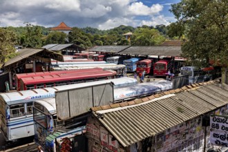 View of a bus depot with numerous parked buses and green hills in the background, Kandy bus station