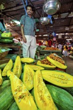 A man stands at a market stall with glowing pumpkin and other fresh vegetables, The old market