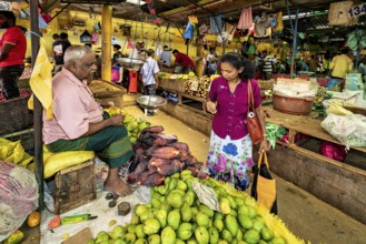 A man and a woman are discussing green mangoes at a colorful market stall, the old market halls of